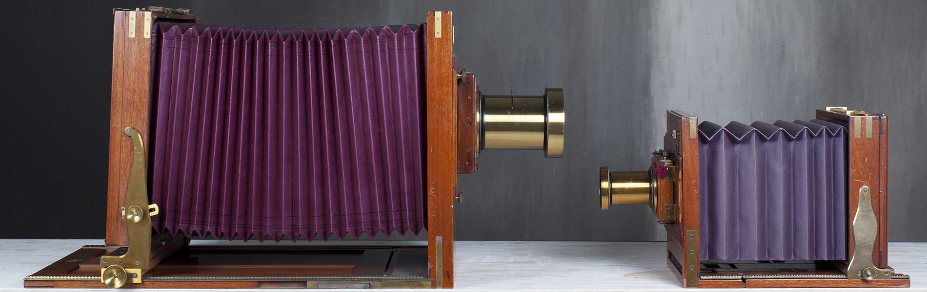 Två bälgkameror som står mot varandea. De ser ut som lila dragspel med ett kikarsikte