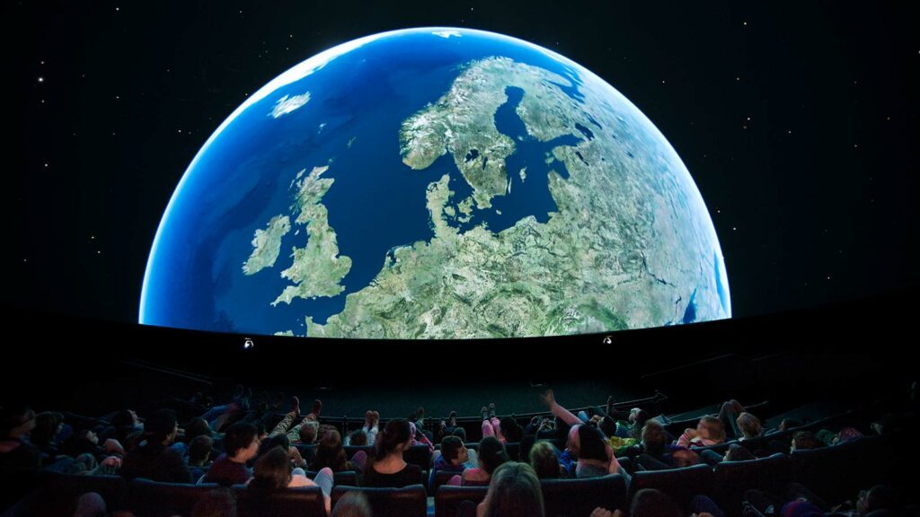 publik som sitter i en dome och tittar på jorden i 3D