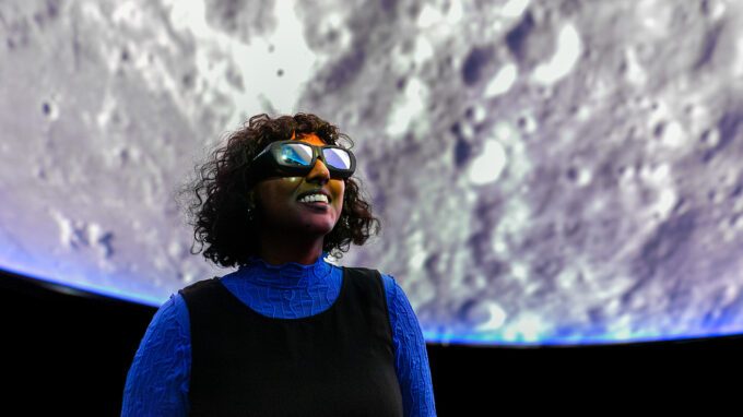 tjej som står framför en visualiseringsdome som projicerar en bild på månen i realtid.