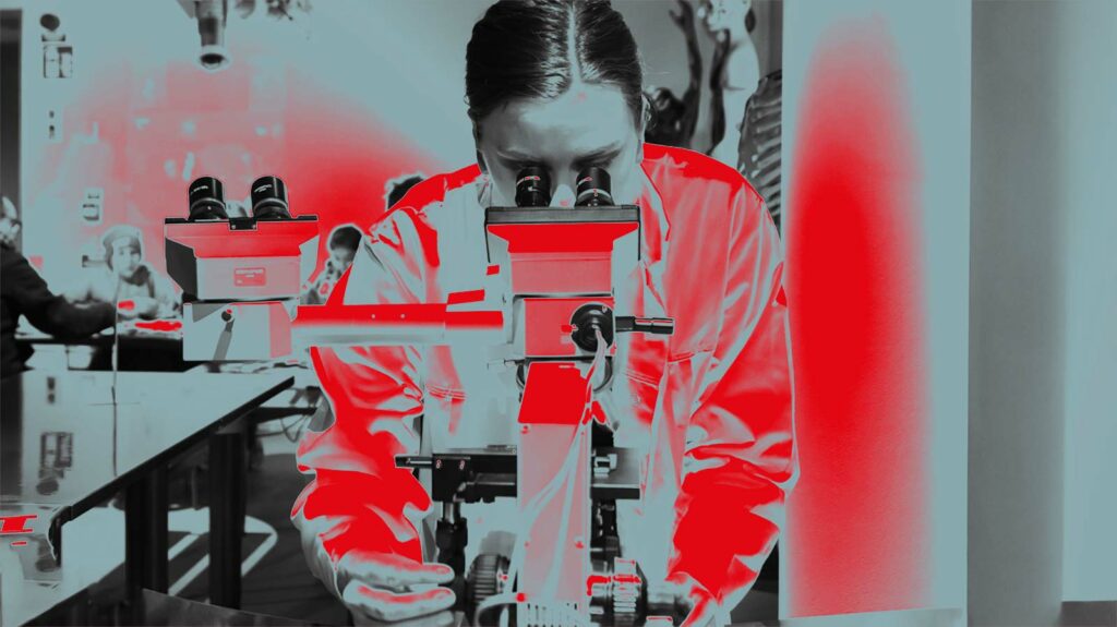 Tjej som kikar genom ett mikroskop klädd i labbrock.