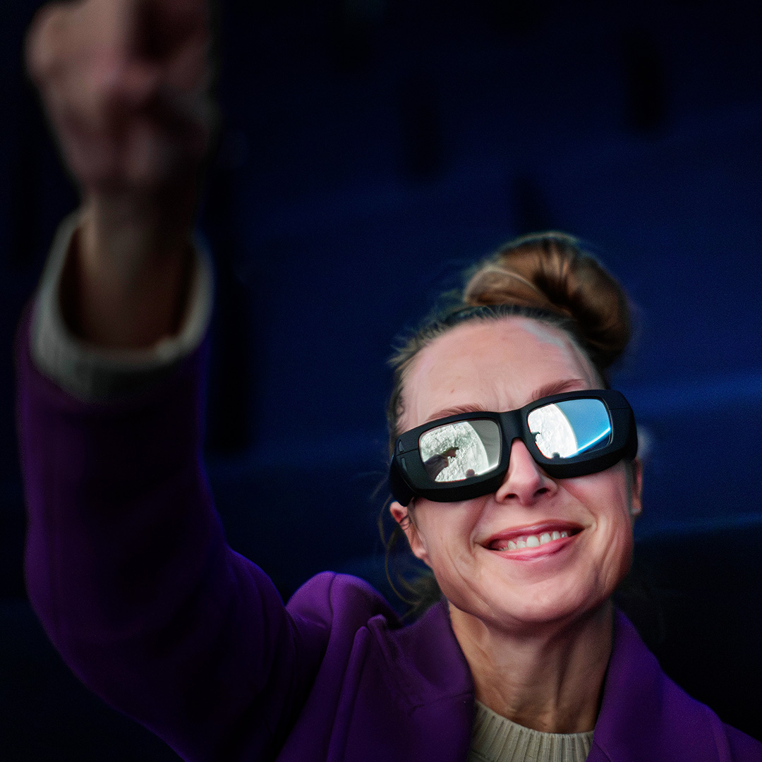 Kvinna som glatt pekar mot skärmen medan hon har på sig 3D-glasögon