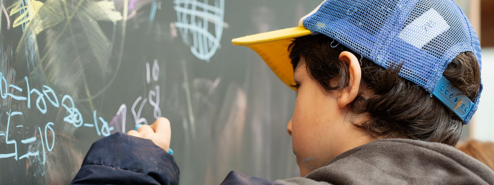 Pojike som skriver med krita på en svart tavla ett mattetal.